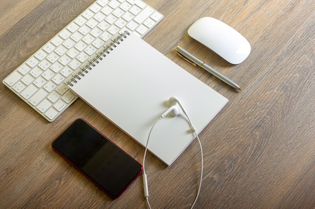notepad with pen and keyboard on wooden table with headphones and smartphone