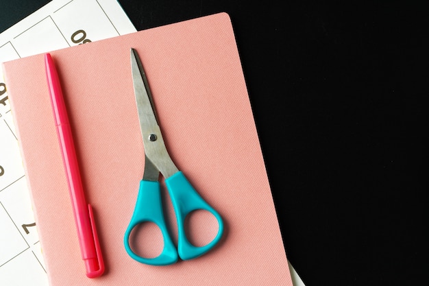 Notepad with pen and scissors on black table close up