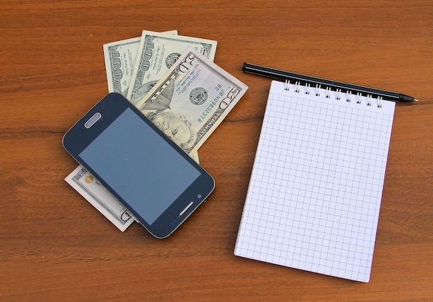 나무 책상에 펜, 스마트폰, 달러 현금이 있는 메모장