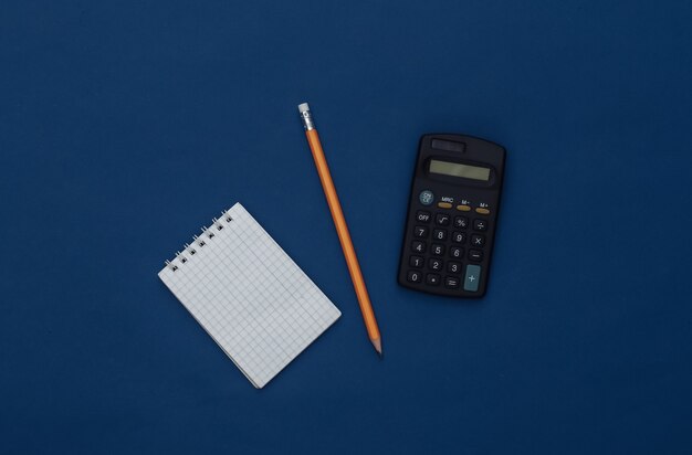 Notepad with pencil and smartphone on a classic blue background. Modern gadgets. Color 2020. Top view.