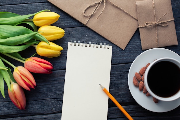 Blocco note con matita accanto a tulipani, caffè e buste.