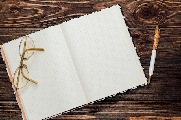 Notepad with reading glasses and a gold pen on a wooden table. Space for text.