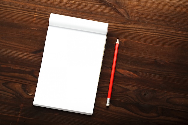 Notepad with red pencil on a brown wooden table background, for education, write goals and deeds