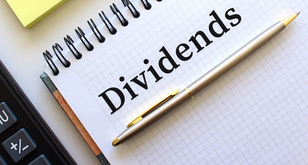 DIVIDENDS 텍스트가있는 메모장 옆에는 계산기와 노란색 메모 용지가 있습니다.