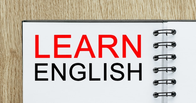 テキスト付きのメモ帳木製の机の上で英語を学びましょう。研究と教育の概念