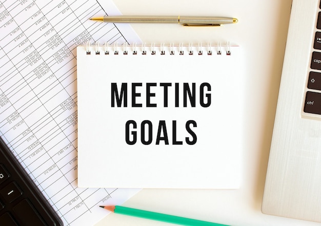 Notepad with text MEETING GOALS on a white background, near laptop, calculator and office supplies. Business concept.