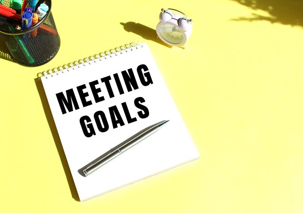 Notepad with text MEETING GOALS with stationery around on  yellow background