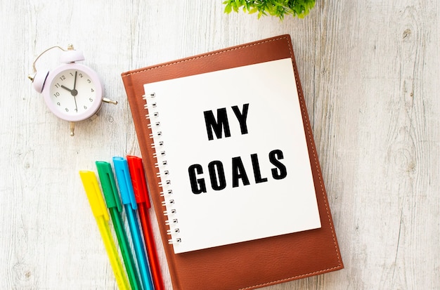 Notepad with the text MY GOALS on a wooden table. Brown diary and pens. Business concept.