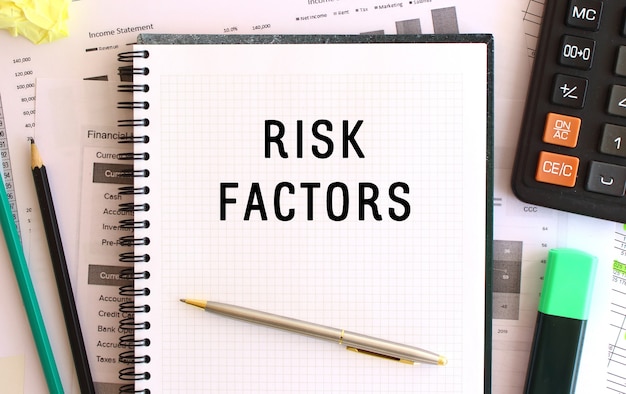 Notepad with text RISK FACTORS on the office desk, near office supplies