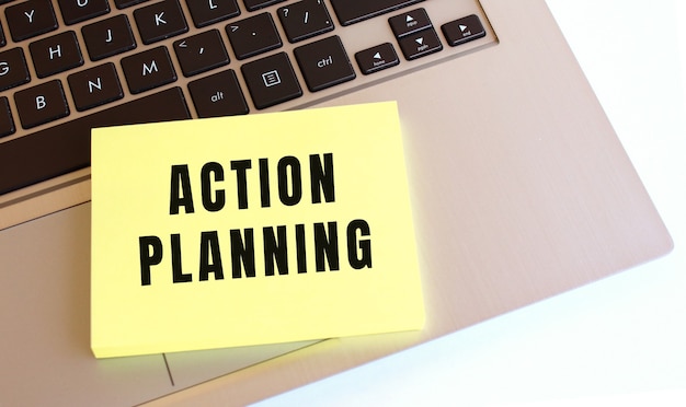 写真 「actionplanning」というテキストが書かれたメモ帳は、ラップトップのキーボードにあります。