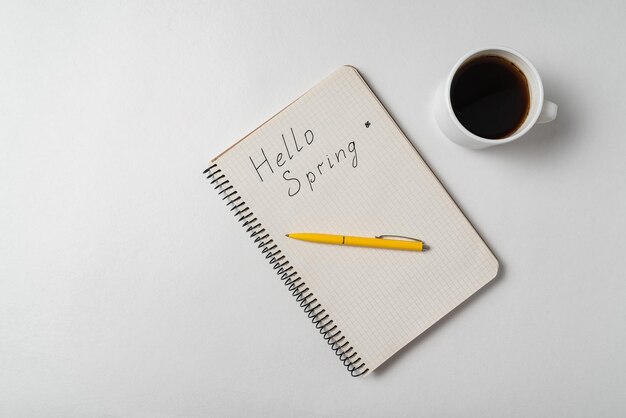 Notepad with the words Hello spring on white background Pen and coffee on notebook Top view