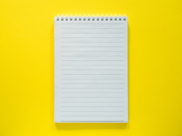 Notepad for writing on the yellow desktop, flat lay, copy space.