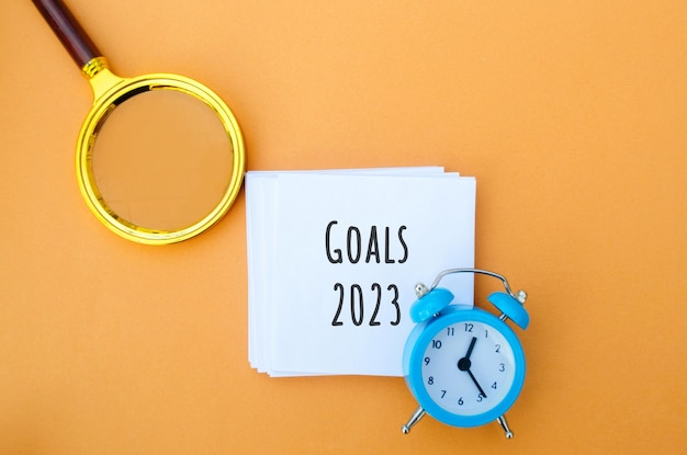 Notes with words Goals 2023 and alarm clock Motivation inspiration Planning plans and tasks New business ideas Setting goal target Magnifying glass