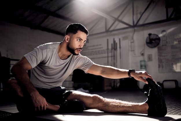 Nothing will work unless you do Shot of a sporty young man stretching his legs while exercising in a gym