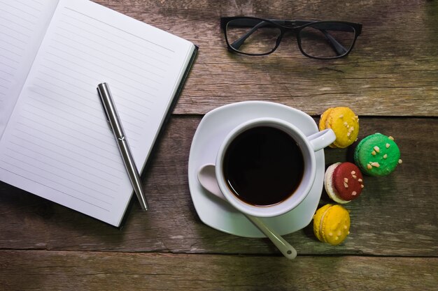 Notitieblok op rustieke hout met macaroon kopje koffie en glazen