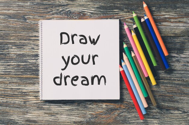 Notitieboek met inspiratie teken je droom en set kleurrijke potloden.