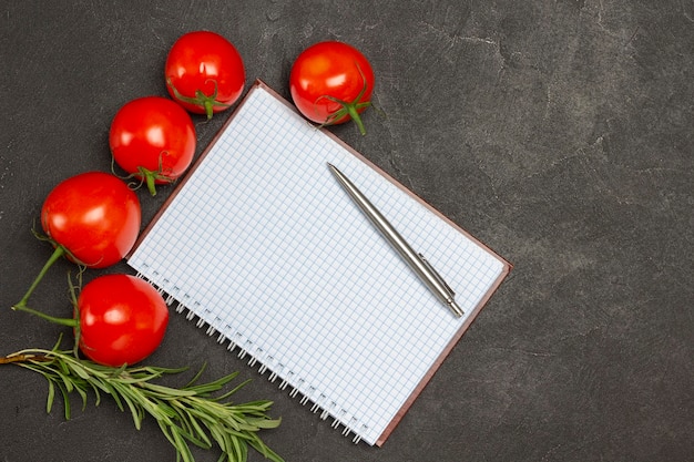 Notitieboekje en pen. Rode tomaten en takje rozemarijn. Zwarte achtergrond. Ruimte kopiëren. plat leggen