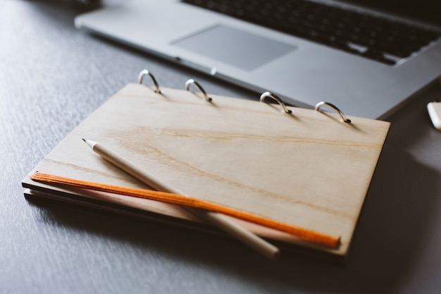 notitieboekje met een houten dekking en een potlood en laptop op een grijze houten lijst