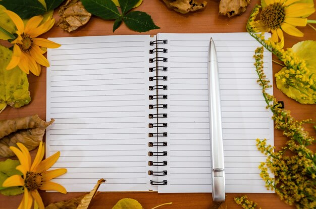 Notitieboekje met een pen in gele herfstbladeren en bloemen.