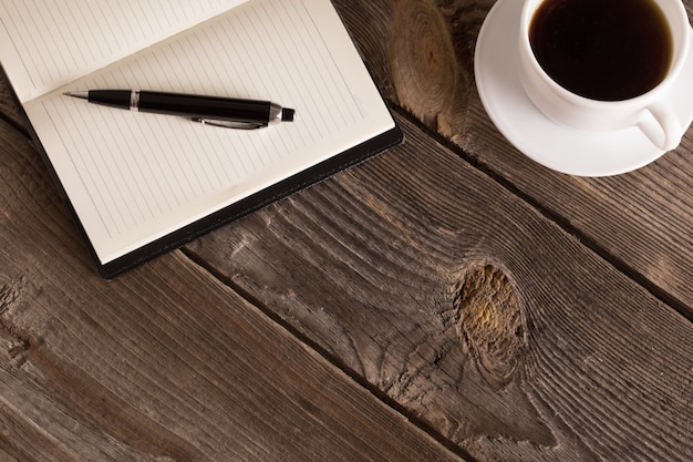 Notitieboekje met pen en koffie op oude houten lijst