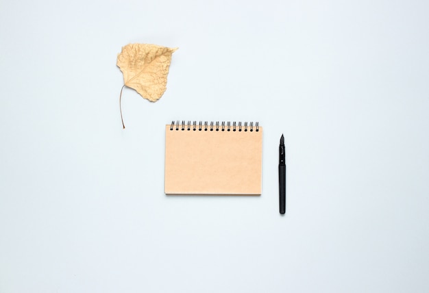 Notitieboekje met pen, gevallen herfstbladeren op een grijze tafel. herfstinspiratie, schrijven. bovenaanzicht, minimalisme. plat liggen