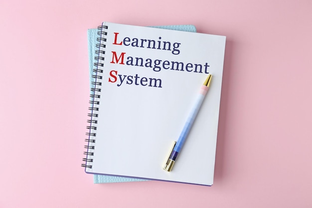 Notitieboekje met tekst Learning Management System en rode beginletters die initialism LMS vormen op roze achtergrond bovenaanzicht