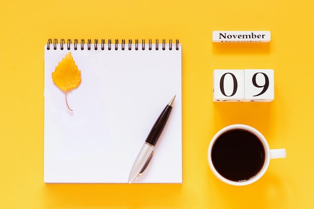 9 ноября чашка кофе, блокнот с ручкой и желтый лист на желтом фоне