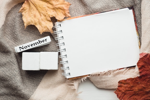 november in calendar made from white cubes on blanket with notebook and leaves. Flat lay