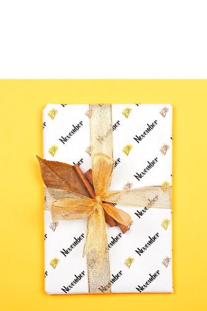 November gift box on bright golden ribbon and autumn leaf