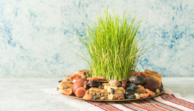 Novruz traditional tray with green wheat grass semeni or sabzi, sweets and dry fruits pakhlava on white background. Spring equinox, Azerbaijan copy space