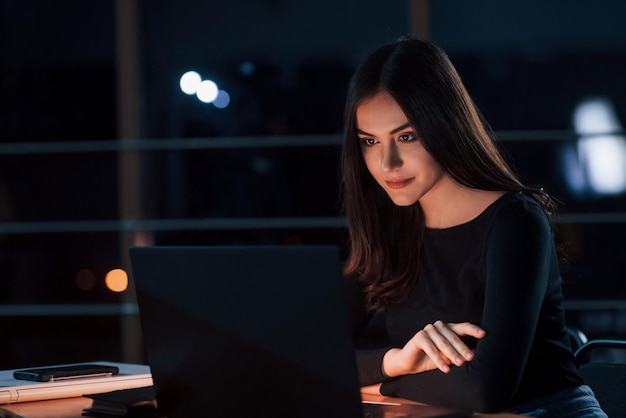 Photo now its time to wait attractive brunette businesswoman works alone in the office at nightime