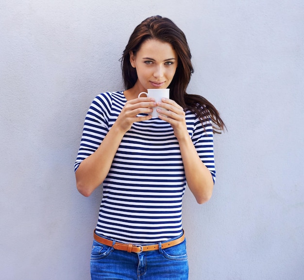 Now thats a fine brew. Portrait of a an attractive woman holding a coffee cup against a gray background.