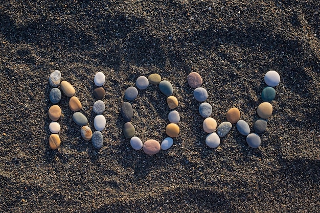 Now word made form stones on sandy beach