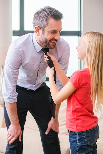 Ora sei pronto per partire. bambina allegra che aiuta il padre a legare una cravatta