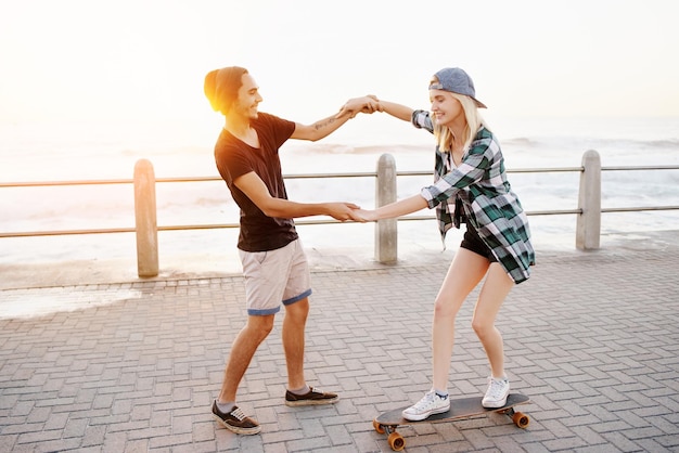 Ora hai capito inquadratura a figura intera di un bel giovane che insegna alla sua ragazza come fare skateboard sul lungomare