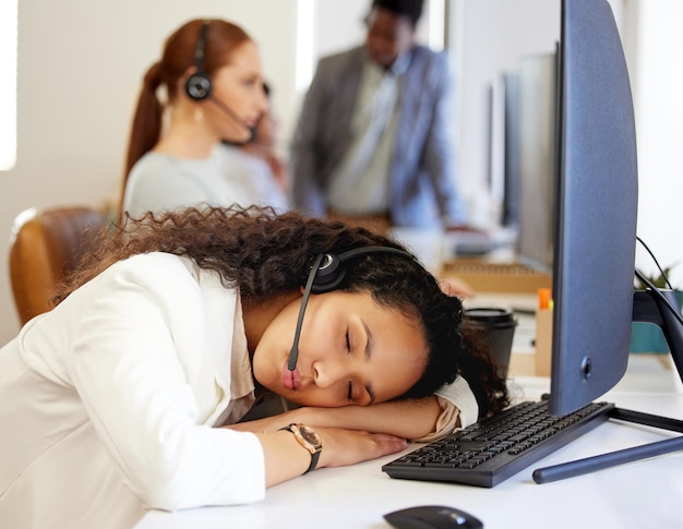 Nu weet je waarom niemand je oproep beantwoordt. Shot van een jonge callcenteragent die aan haar bureau in een kantoor slaapt met haar collega's op de achtergrond.