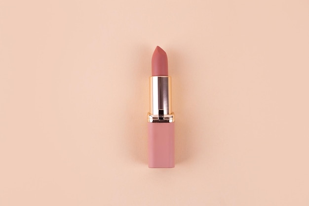 Nude matte lipstick on beige background in pink and gold tube flatlay Professional cosmetic product