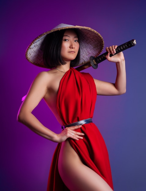 The nude slender Asian woman in a red cape and an Asian hat with a katana in her hand image of a samurai on a neon background