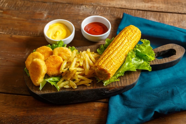 Nuggetsfrietjes en maïskolven op een planksalade op een blauw servet naast kaas