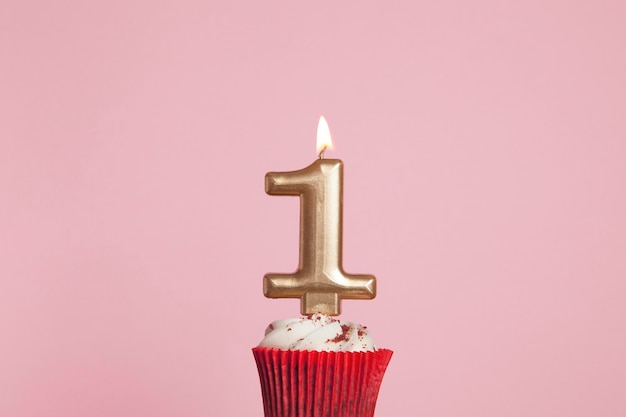 Candela d'oro numero 1 in un cupcake su uno sfondo rosa pastello