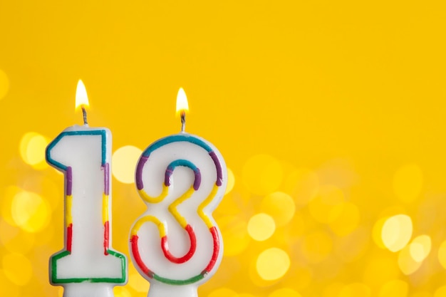 Number 13 birthday celebration candle against a bright lights and yellow background