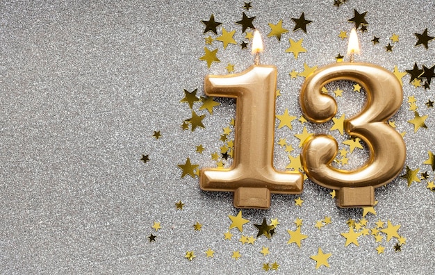 Number 13 gold celebration candle on star and glitter background