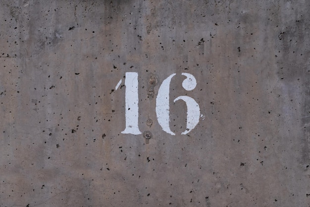 Number 16 drawn on a perforated cement wall, worn\
background