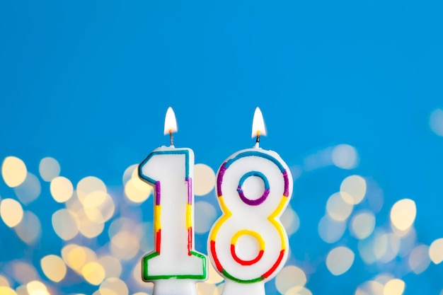 Number 18 birthday celebration candle against a bright lights and blue background