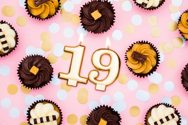 Number 19 gold candle with cupcakes against a pastel pink background