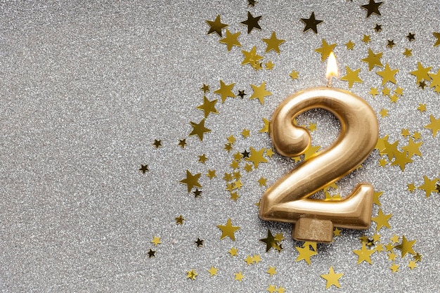 Number 2 gold celebration candle on star and glitter background