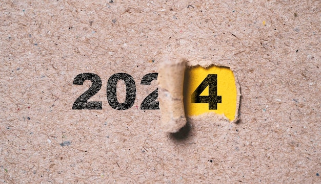 number of 2024 inside of yellow hole of tear paper for change new year from 2023 to 2024 merry christmas happy new year and start new business concept