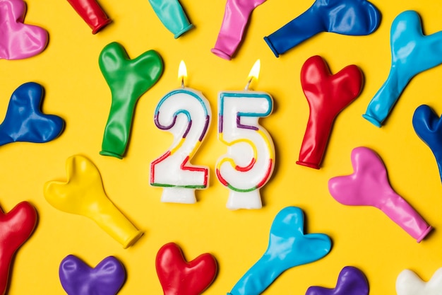 Number 25 candle with party balloons on a bright yellow background