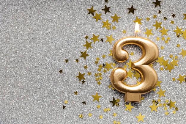 Number 3 gold celebration candle on star and glitter background