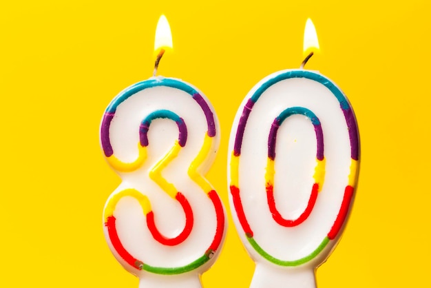 Number 30 birthday celebration candle against a bright yellow background